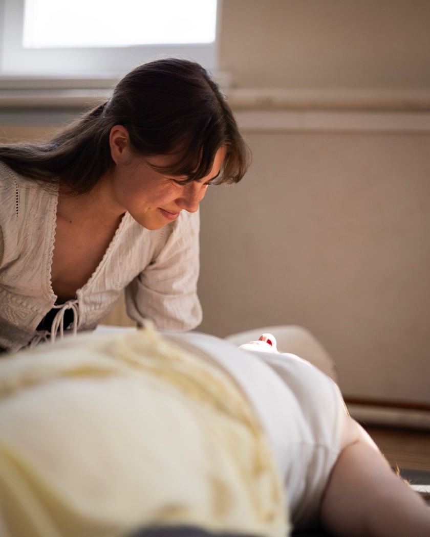 Emi beugt sich während einer Breathwork-Session lächelnd und aufmerksam über eine Person, die auf der Matte liegt.